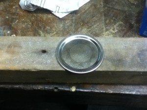 Step one: Place a mason jar lid on a scrap of wood. 