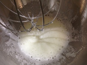 The whipping attachment and the granulated sugar physically change the shape of the egg white proteins transforming the runny raw whites into a fluffy foam.